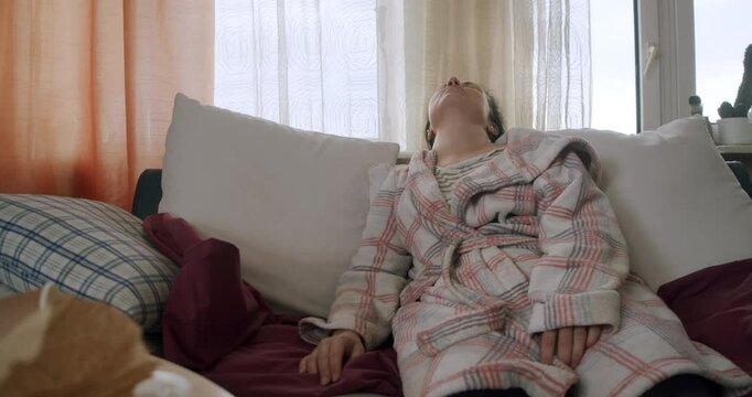 Very tired, exhausted woman sitting on the couch in a mess with no energy. Lazy, unkept woman in a robe want to sleep. Fatigue, tiredness concept. Female mental health concept