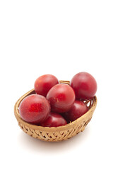 Front view of fresh Cherry Plum (Prunus cerasifera) fruits in a wooden basket on a white background.