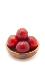 Front view of fresh Cherry Plum (Prunus cerasifera) fruits in a wooden basket on a white background.