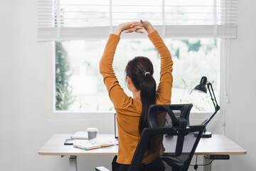 Woman taking a break and stretching at desk in home office.