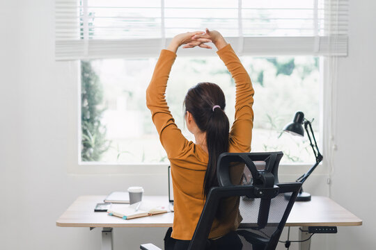 Woman taking a break and stretching at desk in home office.