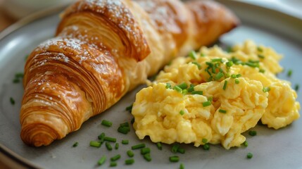 Flaky croissants paired with creamy scrambled eggs, garnished with fresh chives on a ceramic plate.
