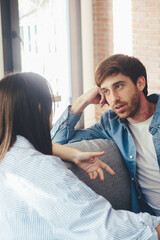 Stressed young married family couple arguing emotionally, blaming lecturing each other, sitting on couch. Depressed husband quarreling with wife, having serious relations communication problems.