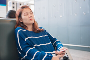 Young Asian tourist woman sleeping on waiting seats. She wait for departure in airport terminal.