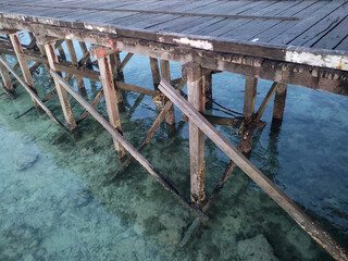 A sturdy wooden bridge in good condition stands over beach shallow waters. Its pillars are covered with many barnacles.