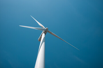 White wind turbine against blue sky. View from the ground.