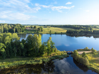 Fototapeta premium A beautiful aerial panorama of a small lake between green summer trees and fields. Natural landscape of countryside in Latvia, Northern Europe.