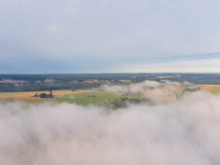 Soft white fog covering the rural summer landscape of Latvia countryside. Aerial photography of mist clouds.