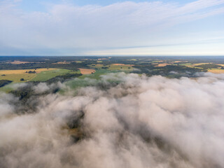 Soft white fog covering the rural summer landscape of Latvia countryside. Aerial photography of mist clouds.