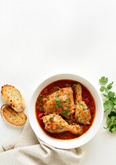 Chicken stew with tomatoes and herbs in bowl over white background with copy space