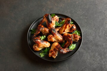 Grilled chicken wings on plate on dark stone background