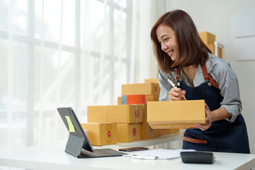 SME entrepreneurs, small businesses Online sales concept, happy Asian female business owner working on laptop computer and parcel boxes. Delivery of SME parcel boxes to customers Confirm order.