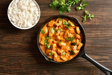 Chicken tikka masala curry in cast iron pan on wooden background