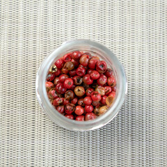 Red or pink peppercorns on wooden spoon on grey textured cutting board background