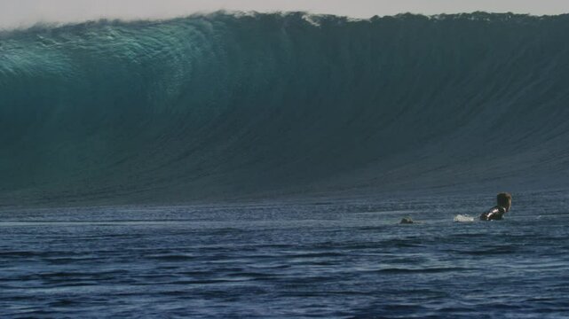 Surfer paddles to get out of impact zone as wave at Cloudbreak Fiji comes crashing down sparkling with mist