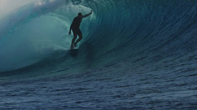 Surfer balances and drags wave as they ride deep in the barrel underneath the lip of wave, Cloudbreak Fiji