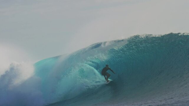 Surfer glides and carves along wave face at Cloudbreak Fiji, slow motion
