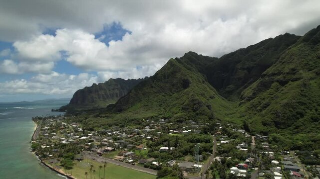 Aerial wide drone video of the small town of Kaaawa, Oahu on the eastern side of the island with the iconic mountains of Kualoa Ranch in the background 