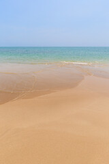 Front view of a small wave crashing on a sandy beach, sea and blue sky on a sunny day. Natural tropical travel and vacation background with copy space.