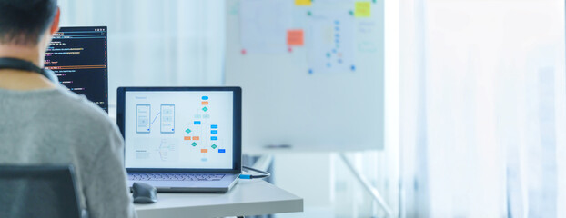 Asian software developers working on multiple screens displaying code and application diagrams in a...