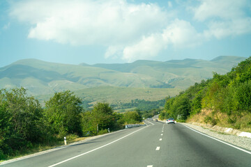 A road with a car driving down it and mountains in the background