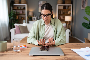 Fototapeta premium Young freelance businesswoman with attention difficulty hyperactivity disorder (ADHD) sitting at home office with laptop computer looking at her fingernails, she cant concentrate and start work.
