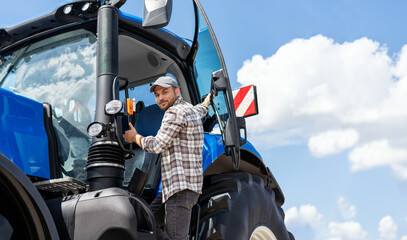 Male  tractor driver gets into the blue farm tractor. © Barillo_Images