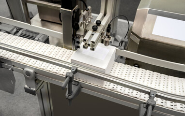 Automatic product labeling and printing solution. White cardboard box on belt of industrial packing machine.