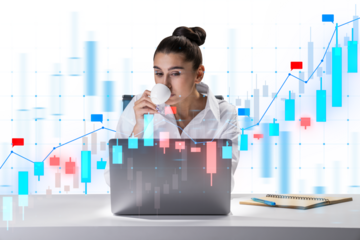 A woman sitting at a desk sipping coffee while looking at a laptop with financial graphs overlaying the image, on a light background, symbolizing analysis