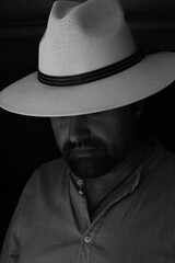 Portrait of a handsome bearded man in a shirt and white hat. The head is lowered down, the eyes are...