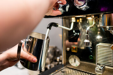 Close-up of a hand frothing milk with an espresso machine steamer.