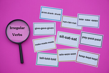 Paper word cards of irregular verbs and magnifying glass. Pink background. Concept, Education....