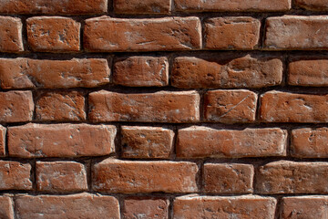 Fragment of a red brick wall, close-up. The texture of brick, battered by wind and rain. Old bricks in the wall of a building.