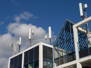 Mobile radio antennas on the roof of a modern office building with gables and spacious windows. Relentless to maintaining the communications network.