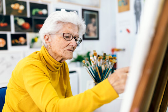 Elderly woman joyfully painting in a bright art studio
