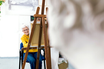 Elderly woman engages joyfully in painting on canvas