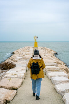 Woman walking towards a yellow lighthouse on a pier in Rimini, Italy