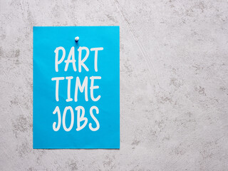 Part time jobs announcement on a blue sheet of paper pinned to a white concrete wall.