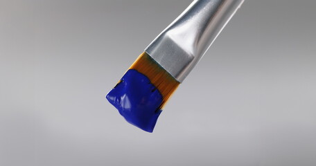 Close-up of brush with blue greasy oil paint on tip, professional equipment for drawing on grey...