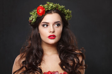 Pretty young woman with floral head wreath looking a side while standing against black background