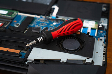 Close-up of a laptop with a red plastic handle screwdriver. Disassemble the computer. Repairing electronic components