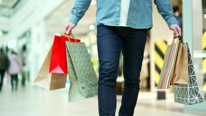 close up man walking in shopping center mall between shops. Unrecognizable shopaholic guy going at store Delighted male with gift packages bag on sale or discount day or black friday indoor plaza