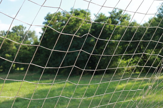 A close-up of a football goal net on a grass pitch with trees in the background. Capturing the essence of local sports.