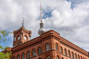 Naklejka premium A large red building with a clock tower and a spire. The building is surrounded by trees and has a cloudy sky in the background