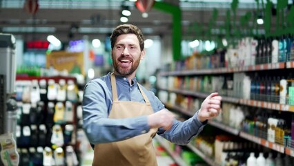 Joyful supermarket salesman worker dancing at marketplace. Happy funny man seller in apron rejoices at workplace between rows of shelves in market grocery store Cheerful glad employee or owner