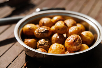 A bowl filled with freshly roasted potatoes sits on a wooden table, bathed in warm sunlight.