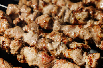 Close-up of skewers of meat, sizzling and grilling over an open flame. The meat is juicy and glistening, with a crispy exterior.