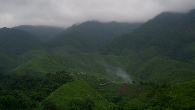 video of beautiful landscape small village on hills around with green mountains with smoke from bonfire and fog