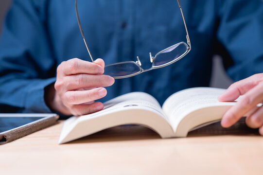Reading book concept. A man is reading a law book with his glasses on. He is wearing a blue shirt. The book is open to a page with a picture of a person