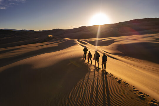 Group of hikers are walking at sunset desert dune. Long beautiful shadows on sand dunes - Powered by Adobe
